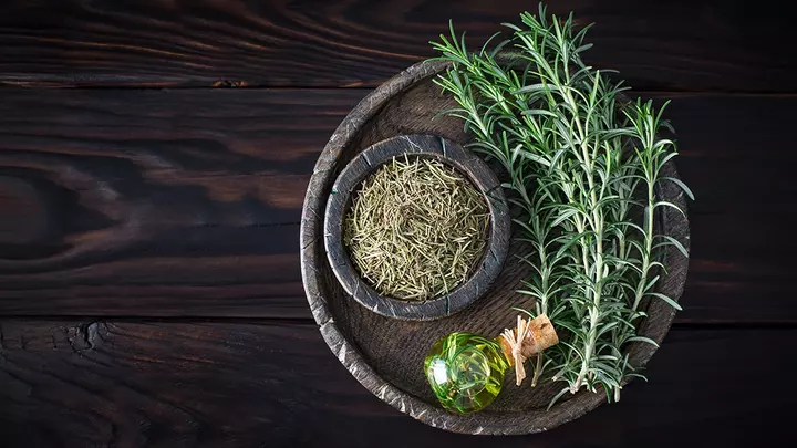 Rosemary oil and rosemary branches on a dark table